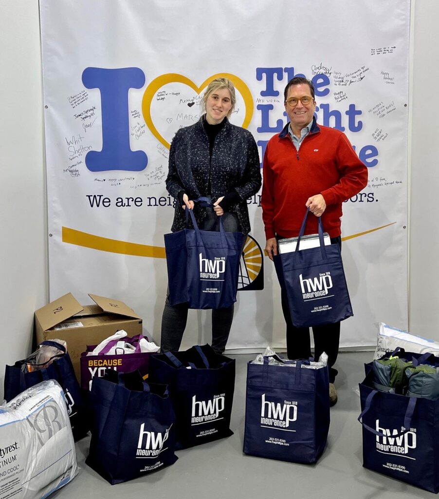 Cherry & Jeff hold donation bags in front of the Annapolis Light House's banner.