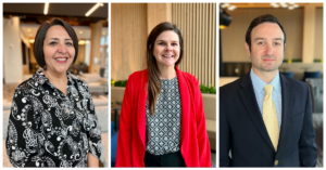 Three new employees posing and smiling in front of an office space.