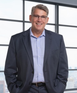 Michael Cauley's Headshot. Michael is wearing a light blue button up with grey sports coat and glasses.