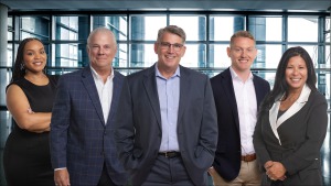 Executive Team Group Photo-Jenaye Matthews pictured far left in a black dress with arms crossed and smiling. Edward Bonifant is to the right of Jenaye and is smiling and wearing a white button down and sports coat. Michael Cauley is pictured center smiling and wearing a light blue shirt, sports coat and glasses. Mark Fleming is to the right smiling, wearing a white button down and sports coat. Barb Beavers is pictured to the far right wearing a black dress with a white collar. She is smiling with her hands held together.